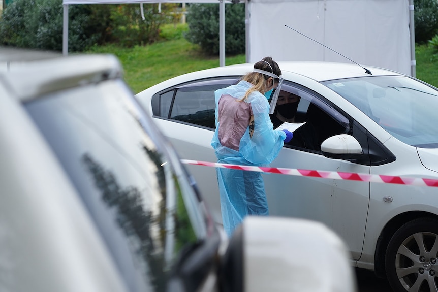 A health worker with paperwork next to a car lined up at COVID-19 testing drive-through clinic at Toowong in Brisbane