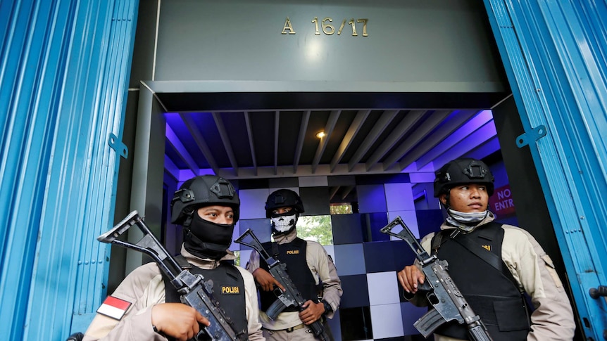Three heavily armed policemen stand outside a men's club in Jakarta.