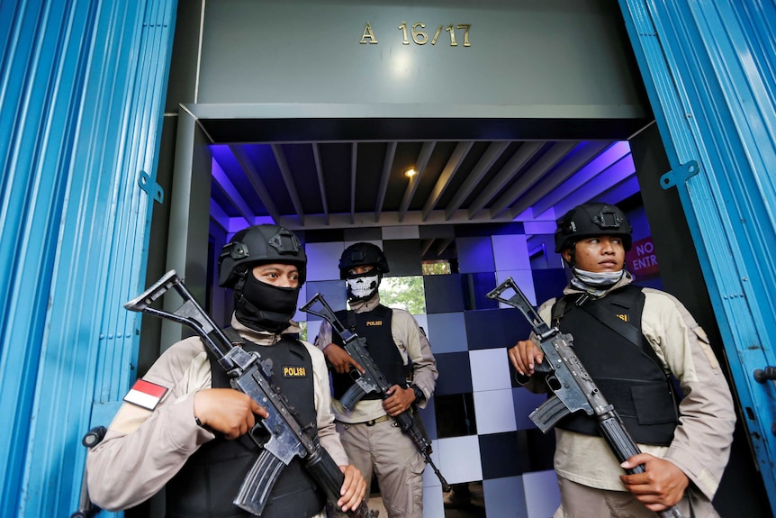 Three heavily armed policemen stand outside a men's club in Jakarta.