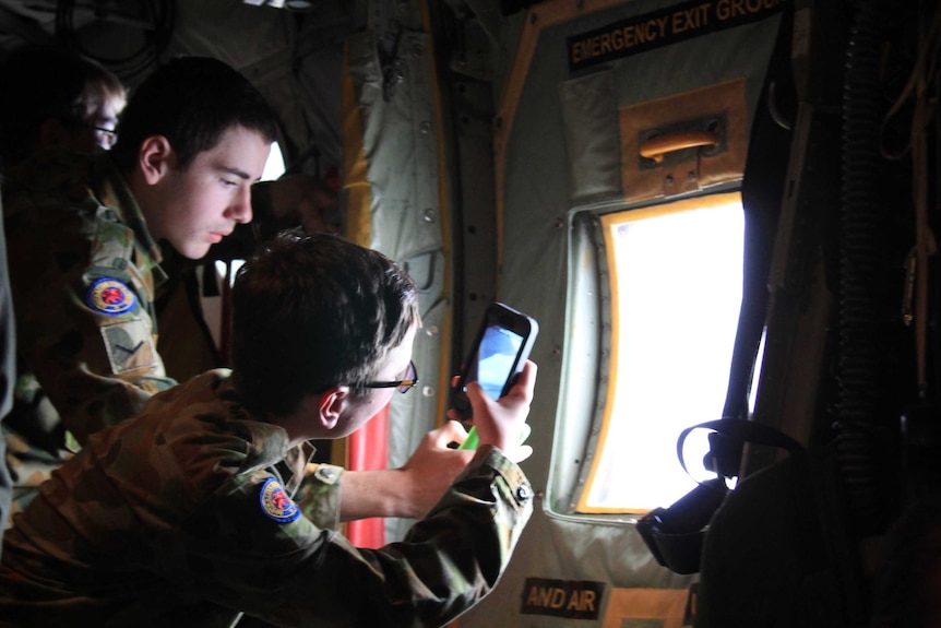 Two young army cadets taking photos on their phones out a plane window