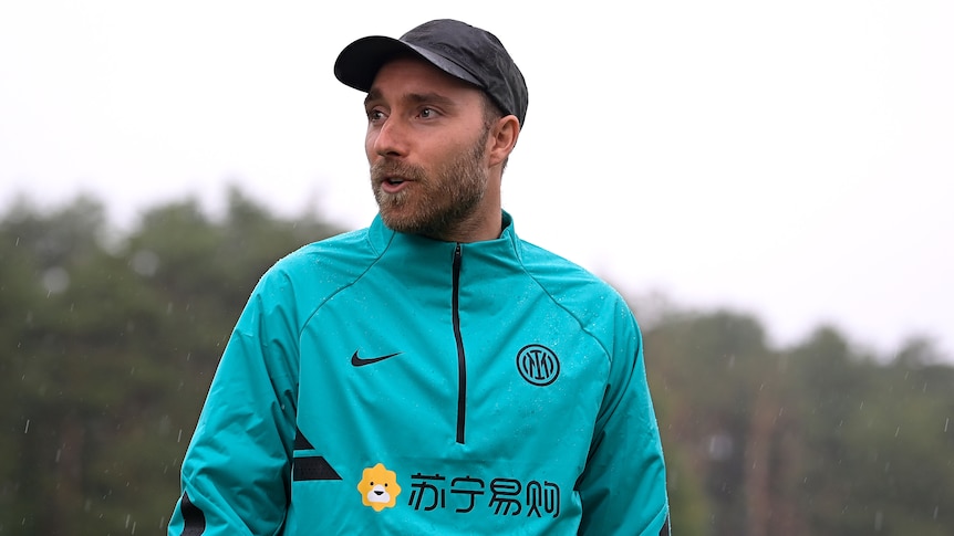 Christian Eriksen looks to one side wearing a cap and rain jacket