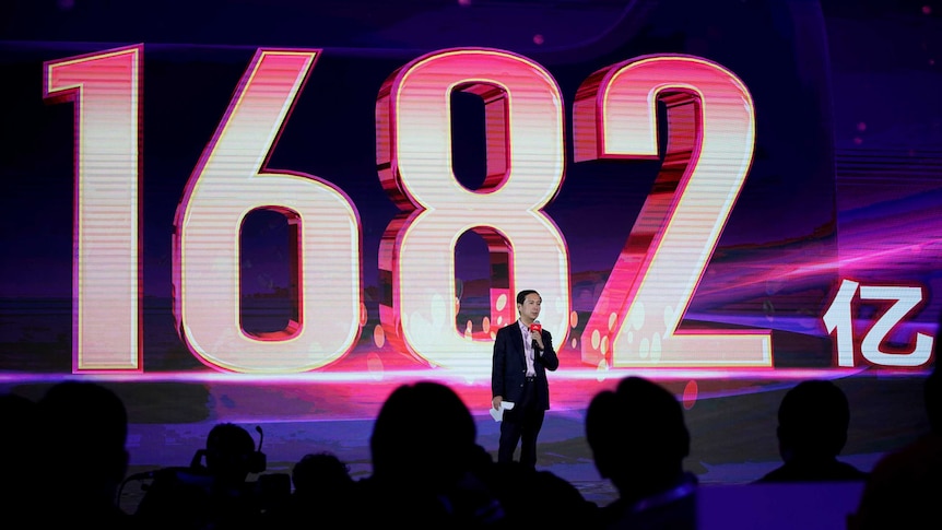 A man stands on stage in front of a giant sign read "1682".