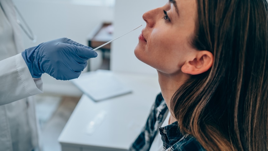 Doctor with protective glove takes coronavirus sample from female patient's nose.