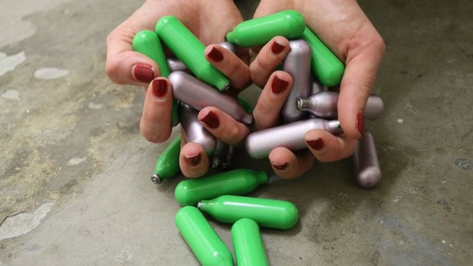 Small green and silver canisters being held in some hands