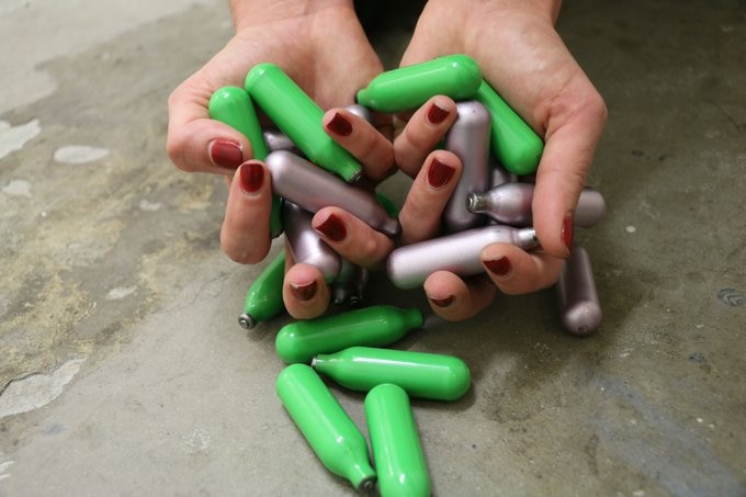 Small green and silver canisters held by several hands