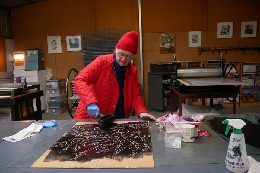 A woman wearing a red jacket rolling a paint brush. 