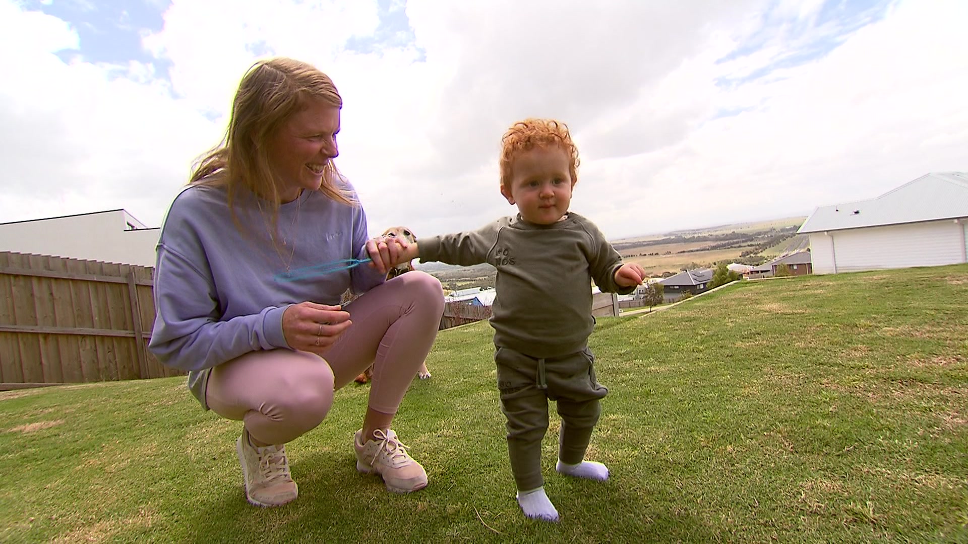 A woman playing with a toddler on a lawn
