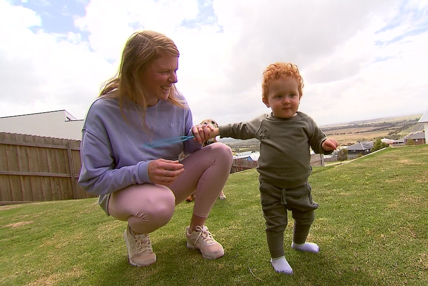 A woman playing with a toddler on a lawn