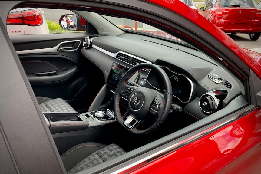 Looking inside a red electric vehicle from the open window, showing the front seat and steering wheel