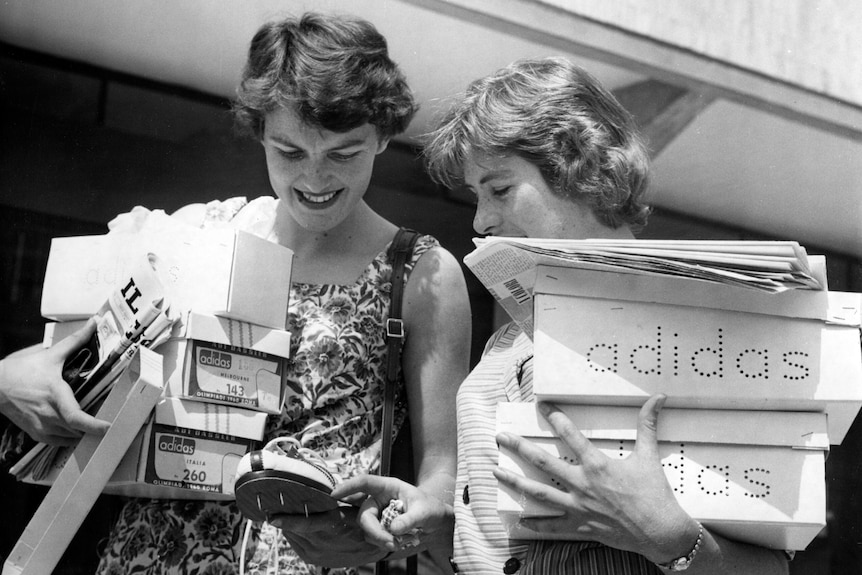 A black and white photo of two female athletes holding Adidas boxes.