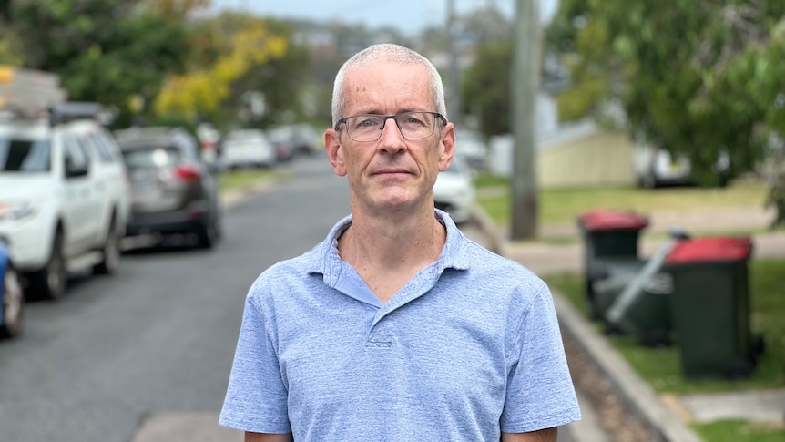 A middle-aged man in a polo shirt stands in a suburban street.