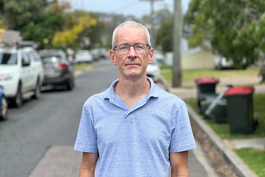 A middle-aged man in a polo shirt stands in a suburban street.