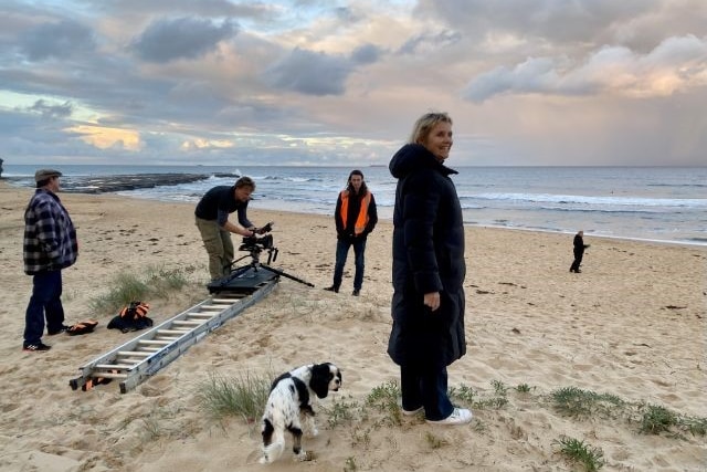 A small crew shoot a film on a beach. 