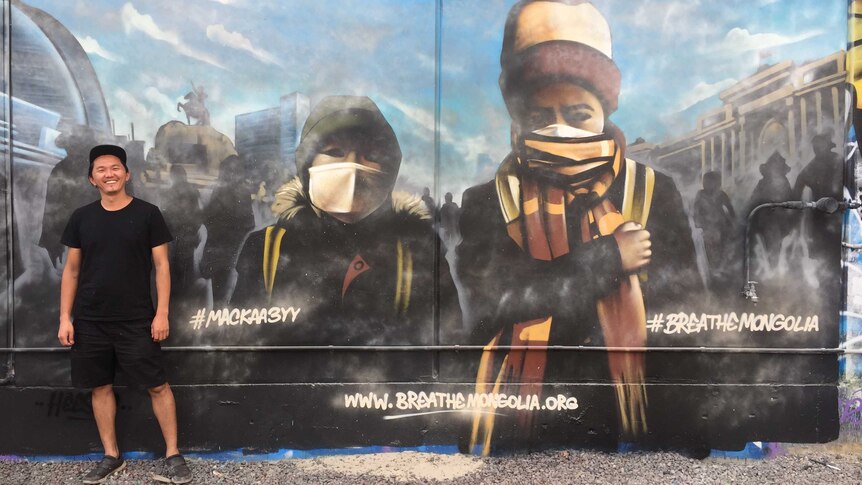 A man stands next to a mural depicting two children in a polluted city.