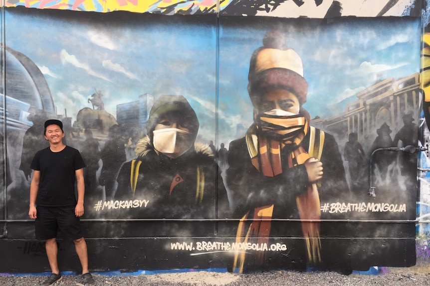 A man stands next to a mural depicting two children in a polluted city.