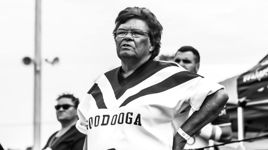 A black and white image shows a woman in a 'Goodooga' NRL jersey with her hands on her hips