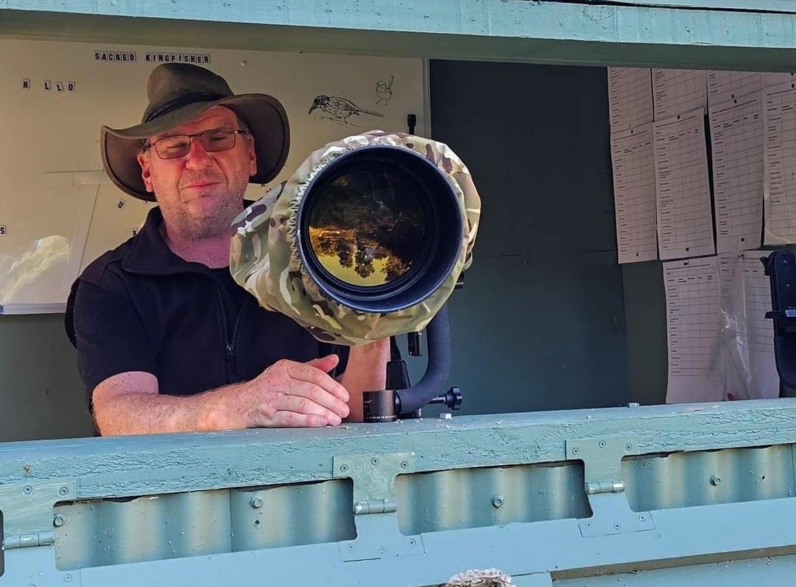 Nature photographer in birdwatching hide with a large camera lens. 