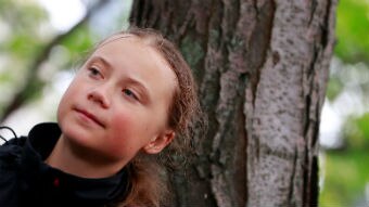 Greta Thunberg stands next to a tree.