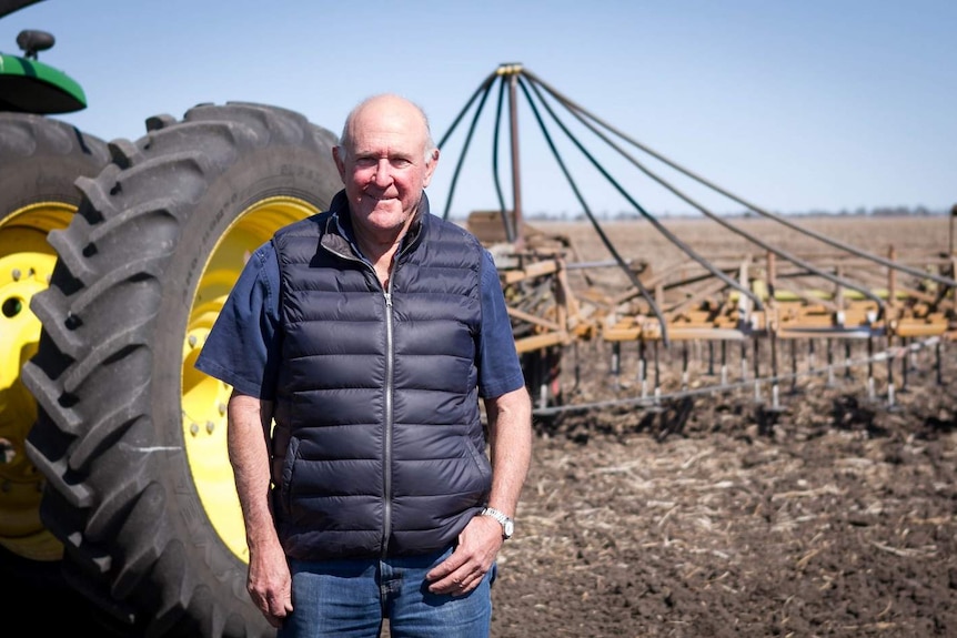 Grain farmer Wayne Newton on a field in front of his tractor.