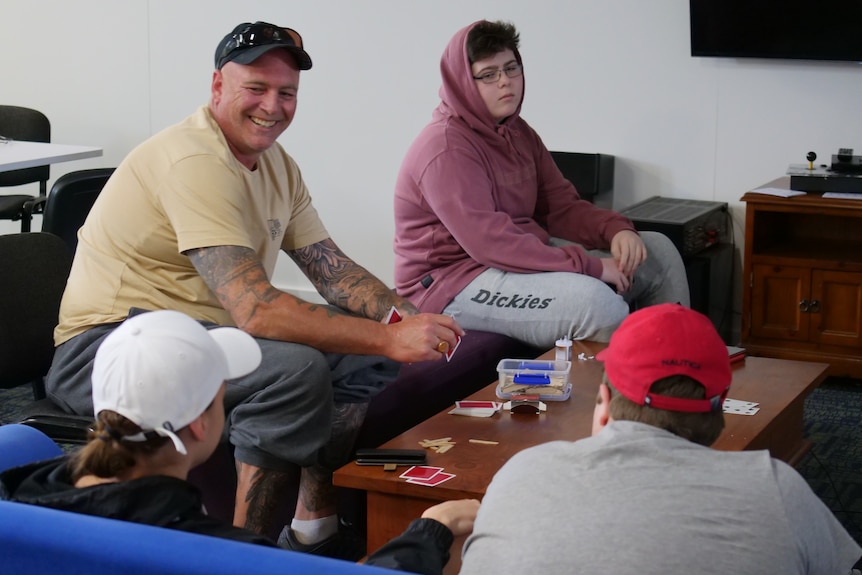 A man and group of teenage boys sitting around a table playing cards.