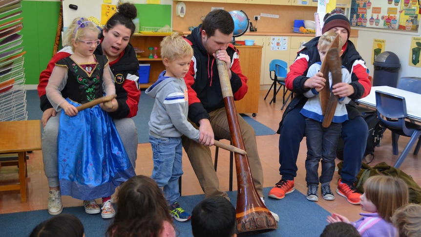 Nakiya, Bevan and Dylan Smith sit in front of a pre-school class playing traditional Aboriginal instruments