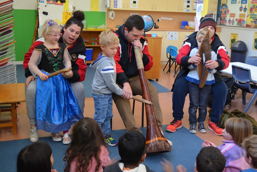 Nakiya, Bevan and Dylan Smith sit in front of a pre-school class playing traditional Aboriginal instruments