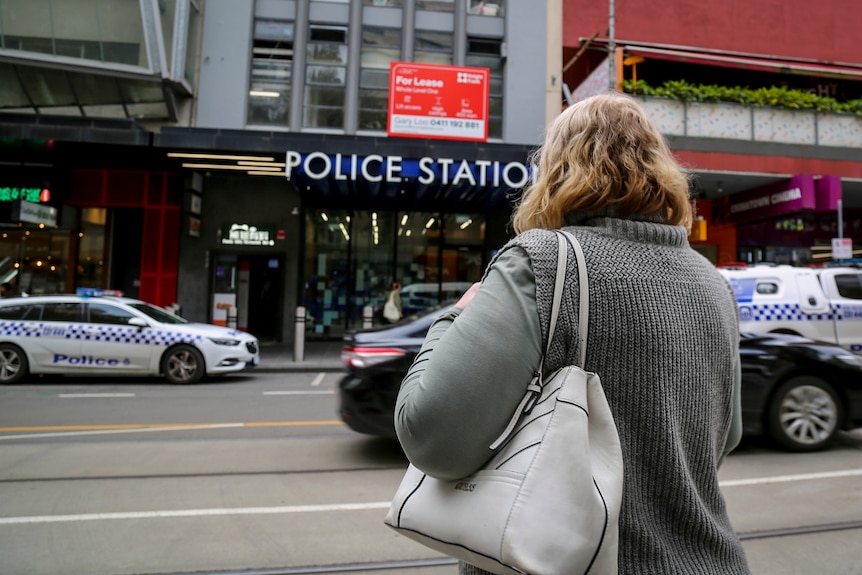 Victoria stands with her back to the camera, looking at a police station which is across a city road.