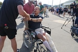 A young man with leg in cast sits in wheelchair shaking hands. 