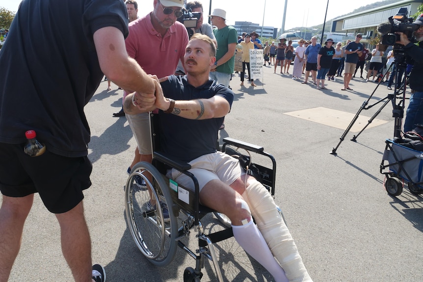 A young man with leg in cast sits in wheelchair shaking hands. 