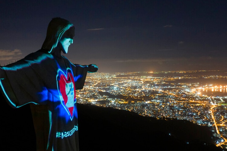 You view an aerial image of Rio de Janeiro at night with the Christ the Redeemer statue lit up with coronavirus messages.