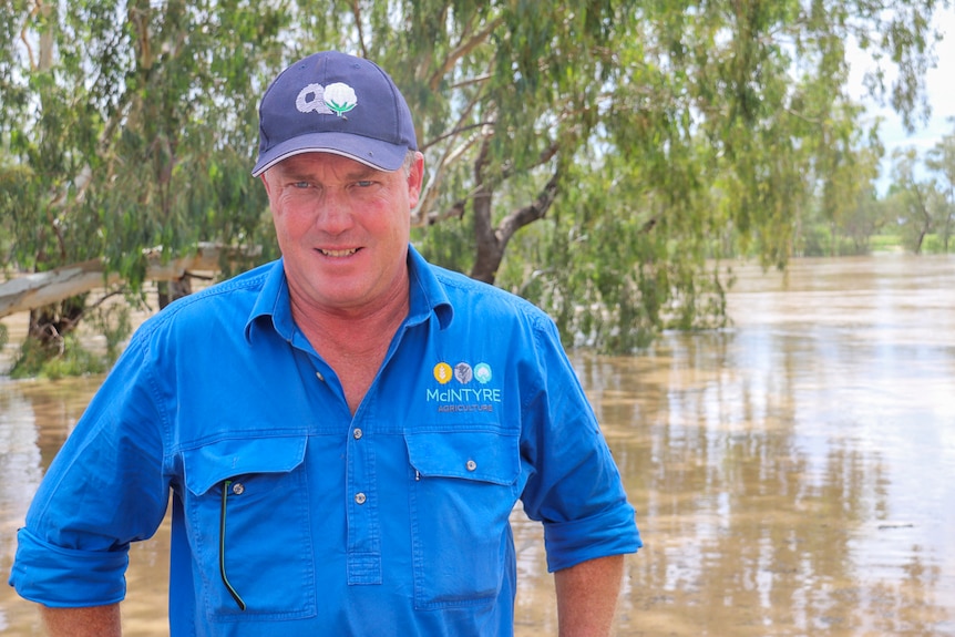 Cotton grower Hamish McIntyre poses for camera in front of brown, swollen river.