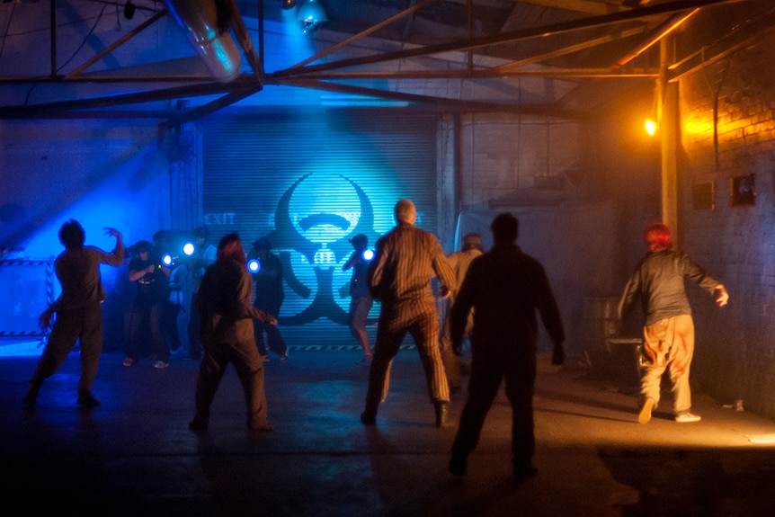 In a warehouse, people dressed as zombies march towards gamers equipped with replica guns