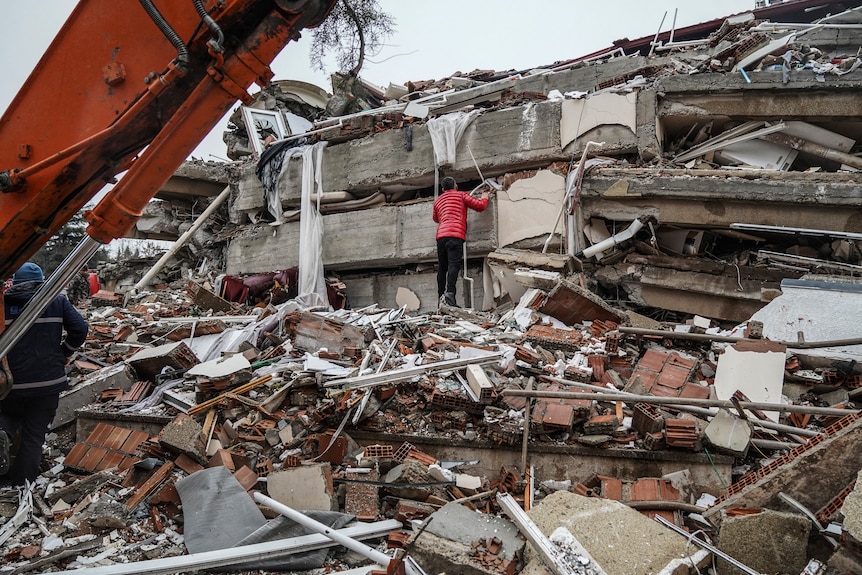 A man searches for people in the rubble of a building.