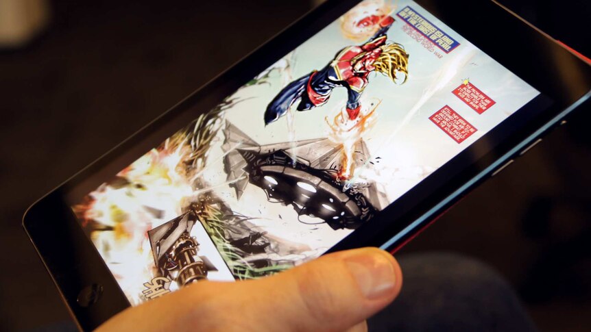 A hand holds an iPad. On it is a page of a Captain Marvel comic book, showing the superhero fighting.