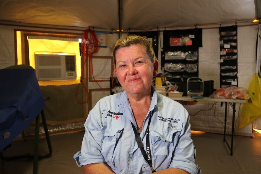 An AUSMAT health worker smiles at the camera. She's in a tent and there is lots of equipment behind her.