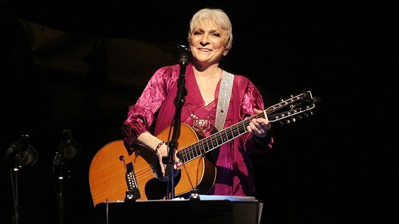 Standing woman in pink top playing twelve string acoustic guitar on stage
