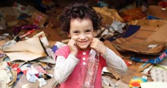 A young girl smiles as she stands among rubbish at a garbage dump in Cairo.