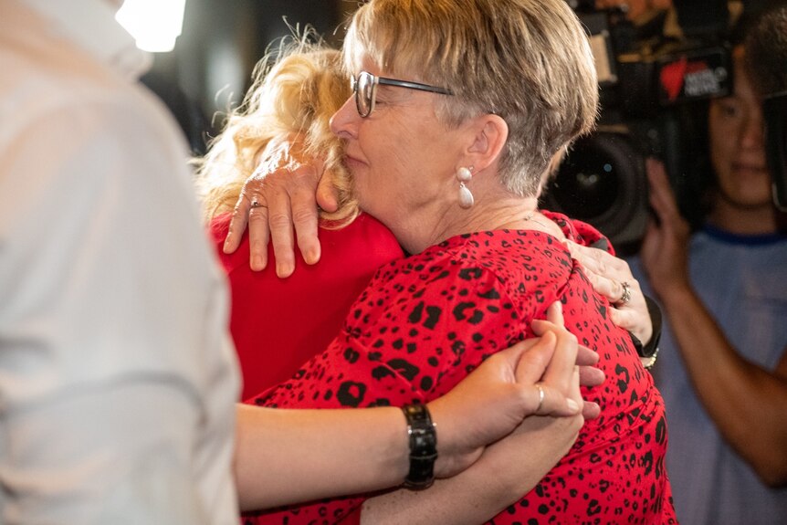 Two women, both wearing red, embrace