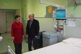 An older man and woman stand in an old hospital room