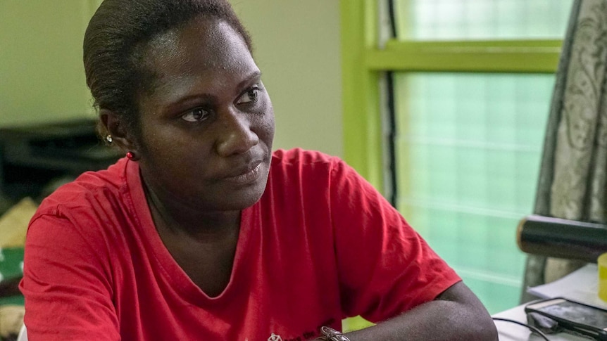 A Papua New Guinean woman in a red t-shirt sits at a desk