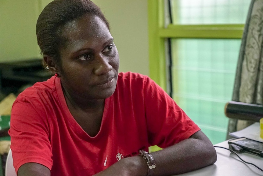 A Papua New Guinean woman in a red t-shirt sits at a desk