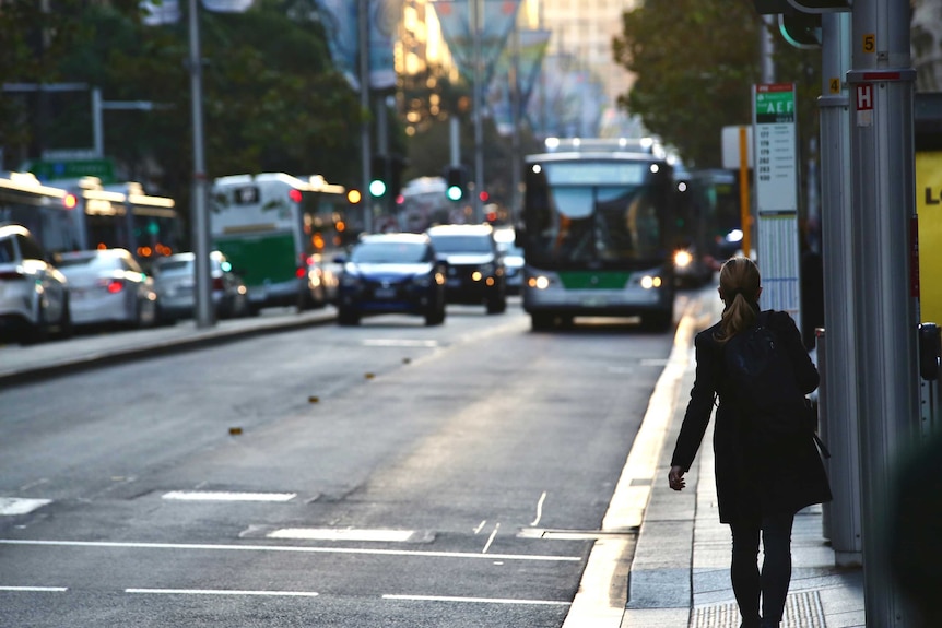 A woman waits for a bus as traffic approaches in the distance looking out over St George's Terrace, Perth