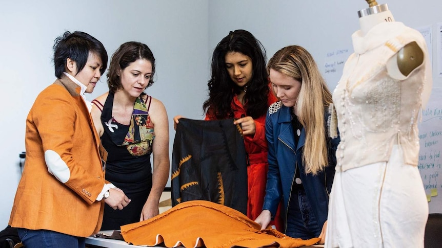 Four students at Queensland University of Technology's fashion school look at some fabric.