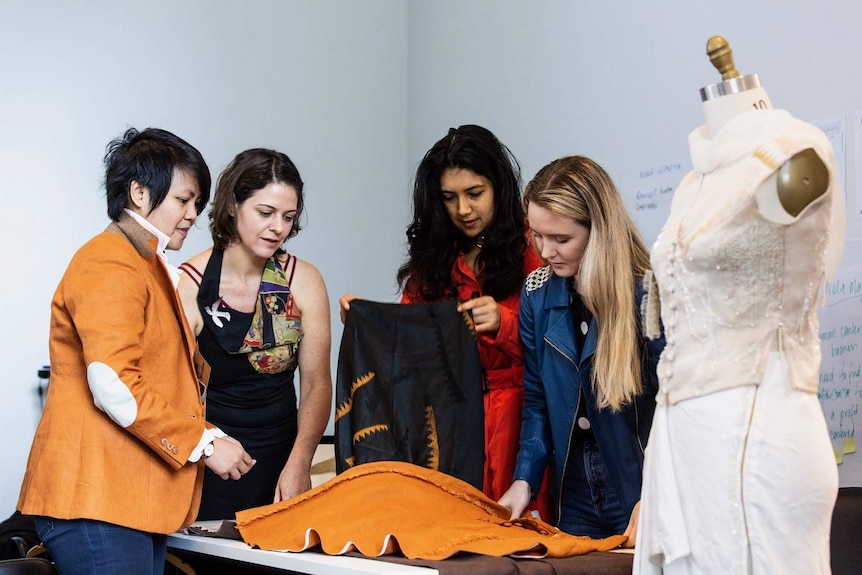 Four students at Queensland University of Technology's fashion school look at some fabric.