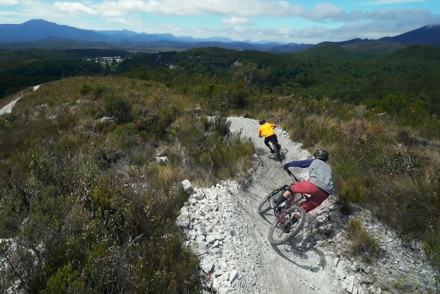Two mountain bikers angling through banked corners for speed.