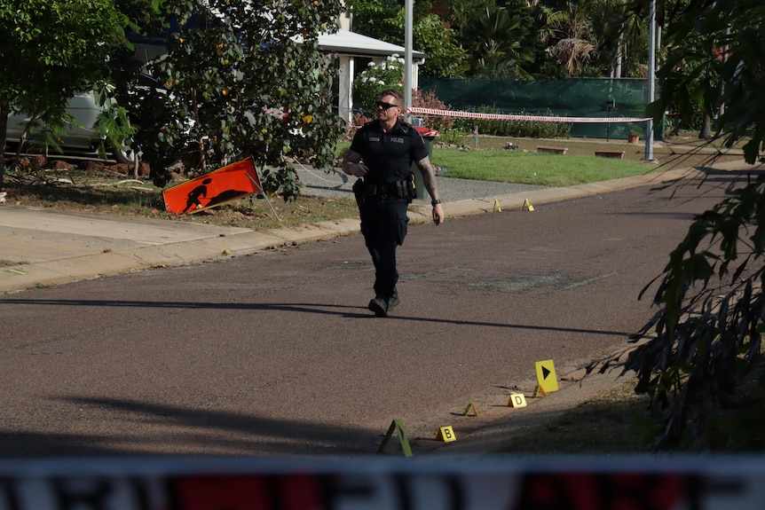 A police officer walks down the road with evidence markers around his feet