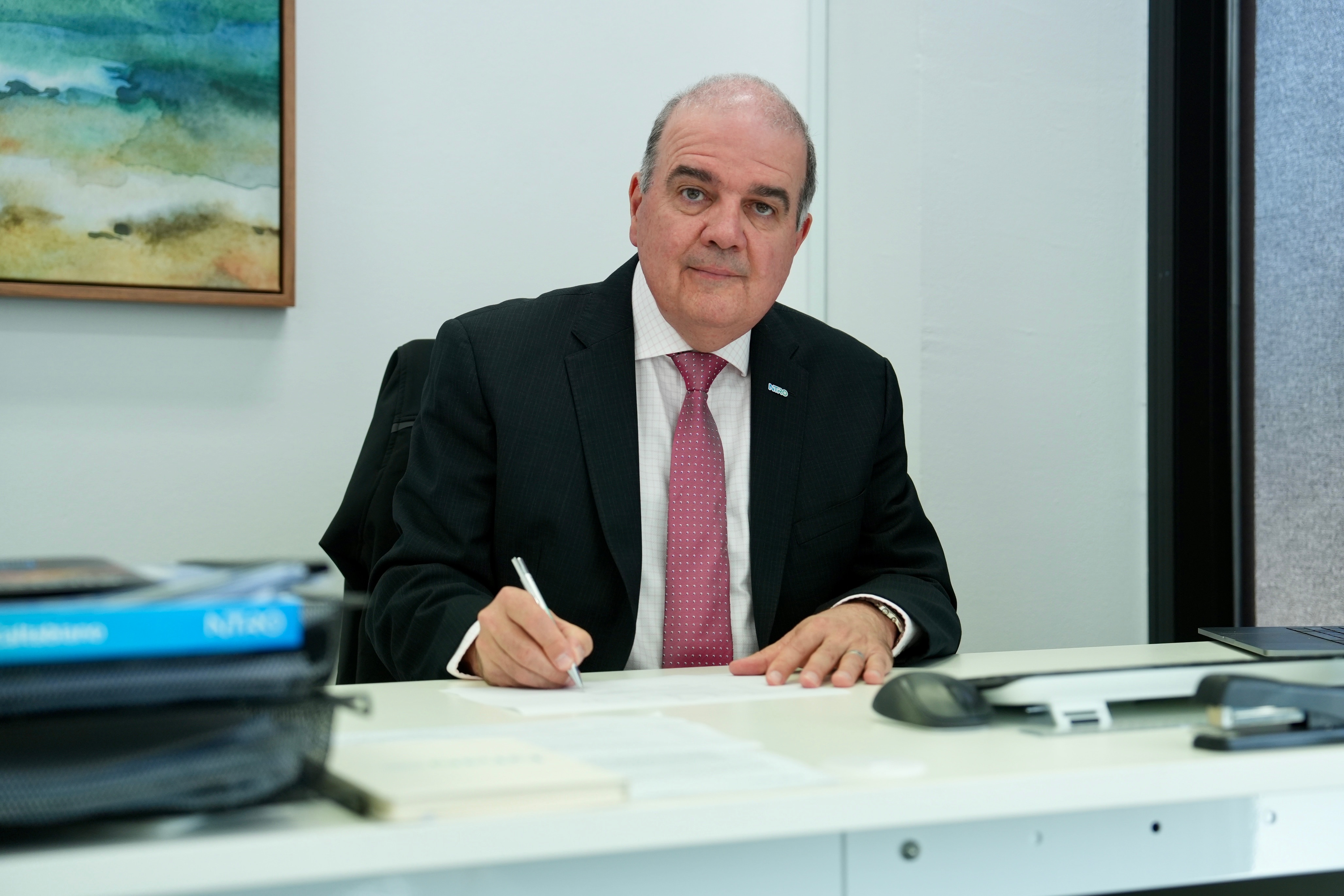 A man sits in a suit and tie looking toward the camera. 