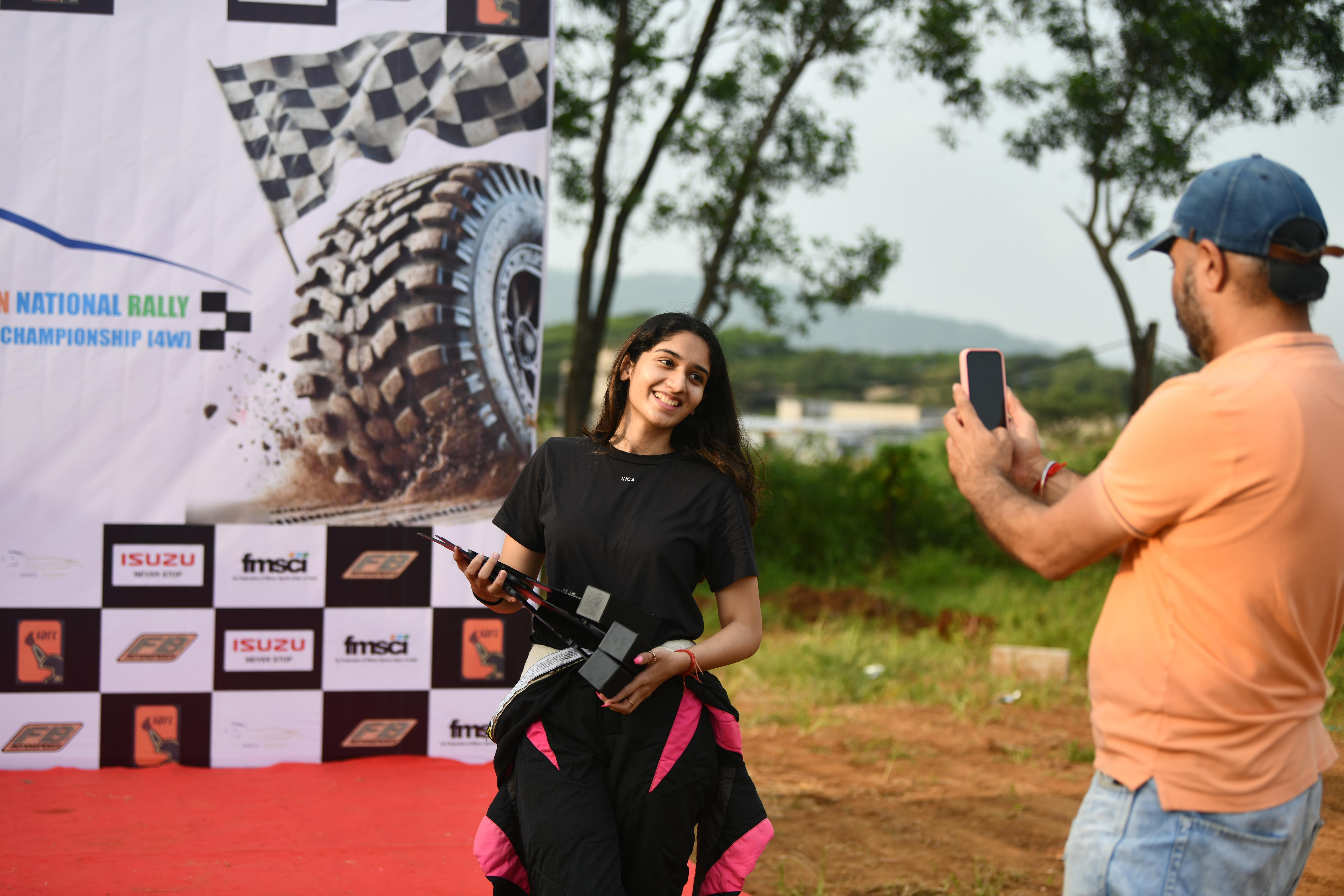 A teenage girl holds a trophy and smiles while a man takes a photo on his camera.