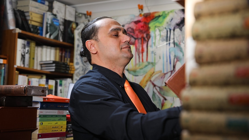 Madhi stacks books while wearing an orange tie and navy business shirt