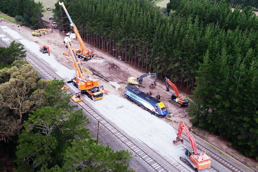 An aerial view of two large cranes preparing to lift a locomotive off the train tracks.